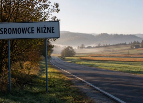 Drogowskaz z nazwą małopolskiej wsi na tle jesiennych wzgórz i pól.